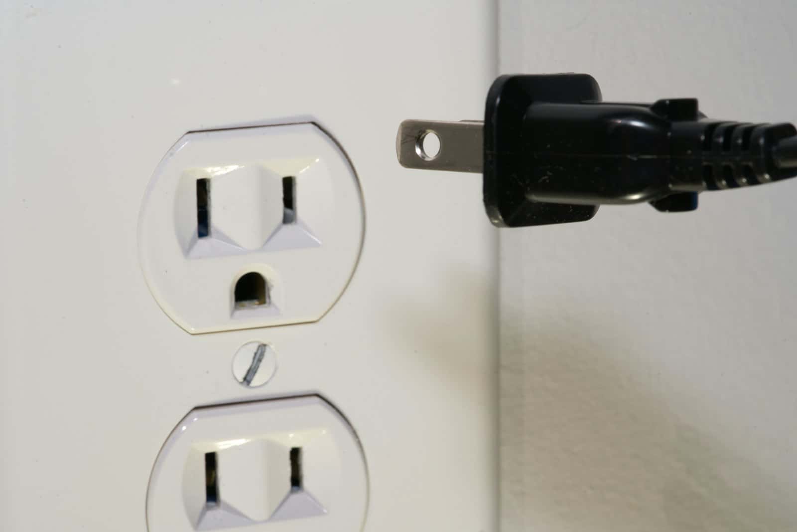 A black plug held in front of a wall socket