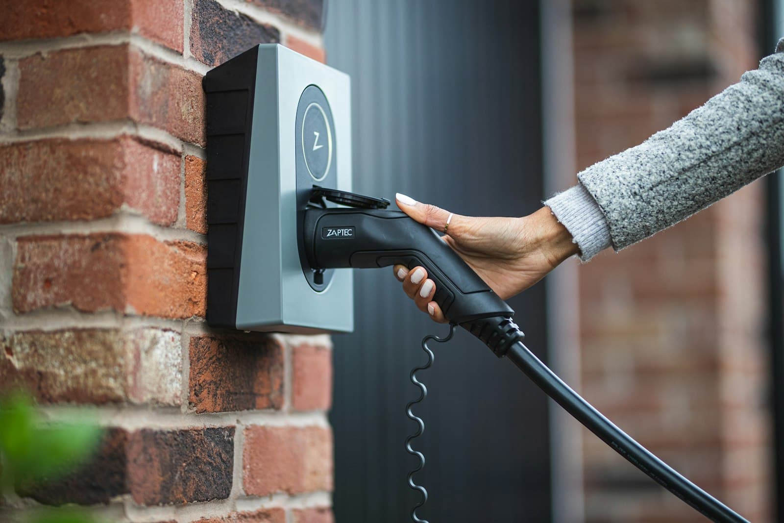 A home EV charger on a brick wall, the cable being plugged in