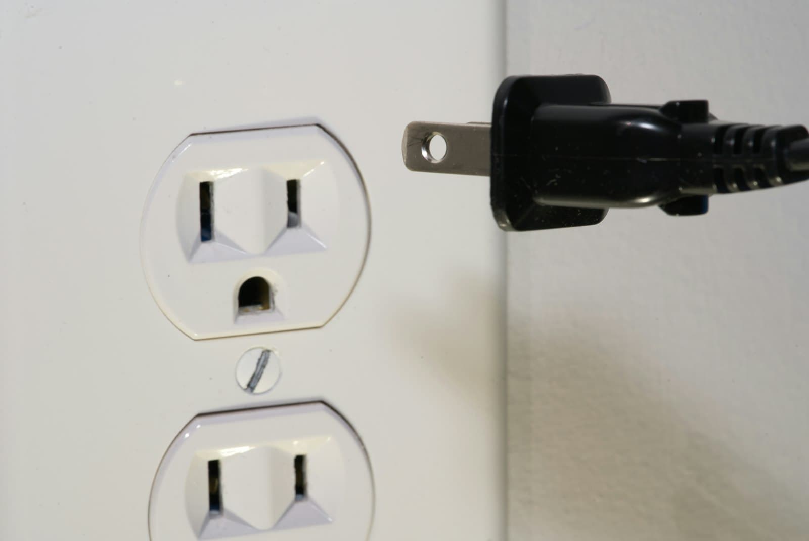 A black plug held in front of a wall socket